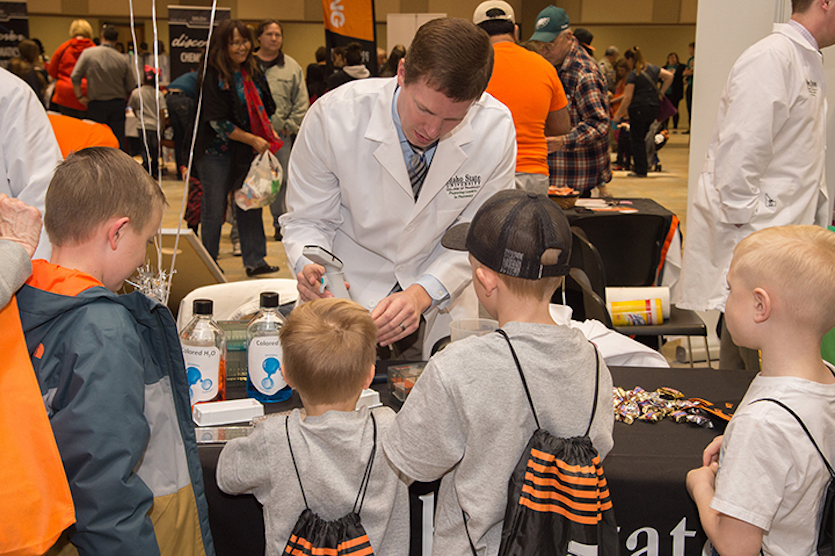 Photo of kids at a booth manned by a guy in a white coat