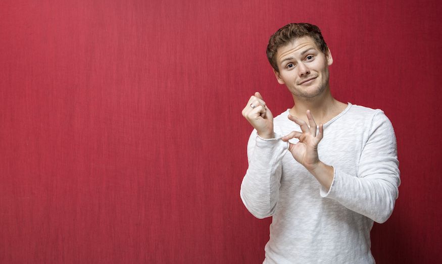 Photo of Drew Lynch standing with a red background