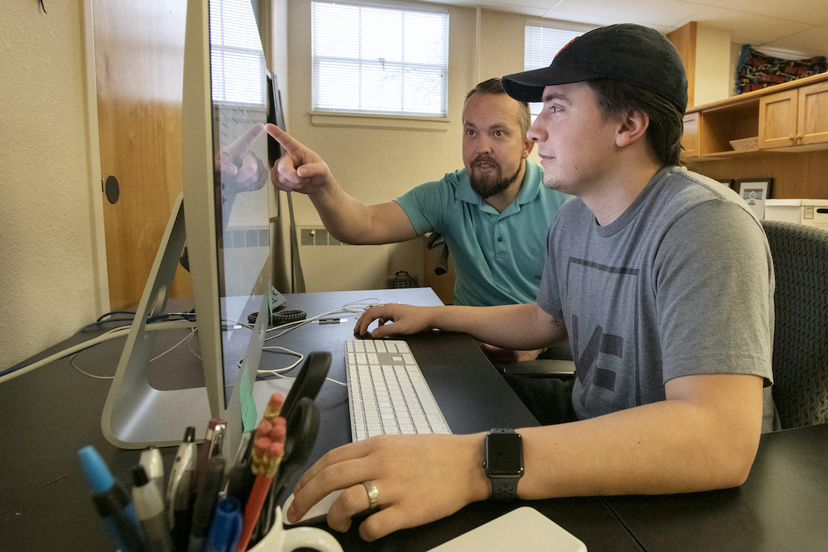 Photo of CPI working on a computer with his supervisor looking on.