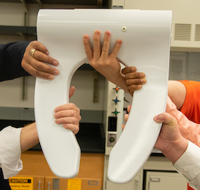 A Washie toilet seat being held up with five hands.