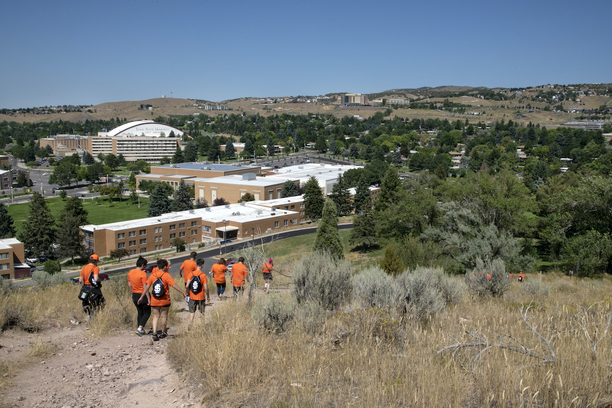 Students in orange shirts walking down a Red Hill trail.