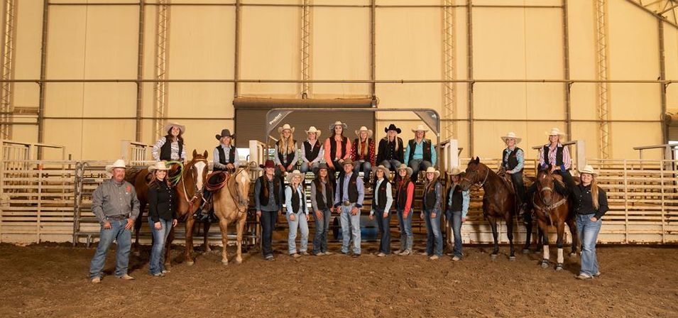 Rodeo team and some horses in front of a large barn.