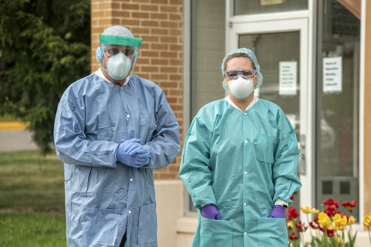 Two volunteers with medical masks and gowns standing outside testing site.