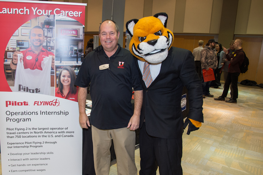 Photo of Benny the Bengal dressed in a business suit standing next to a vendor at the 2018 Career Fair.