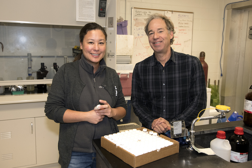 Photo of Ph.D. student Amy Commodore and her advisor Bruce Finney in the ISU Stable Isotopes Laboratory, pictured with some samples of owl pellets in small jars.
