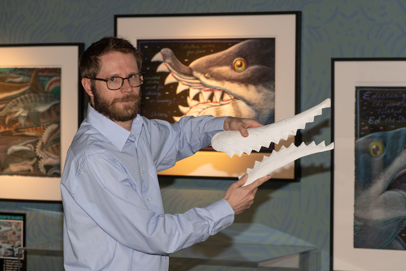 Photo of IMNH director Tapanila with replicas of scissor-toothed shark jaws.