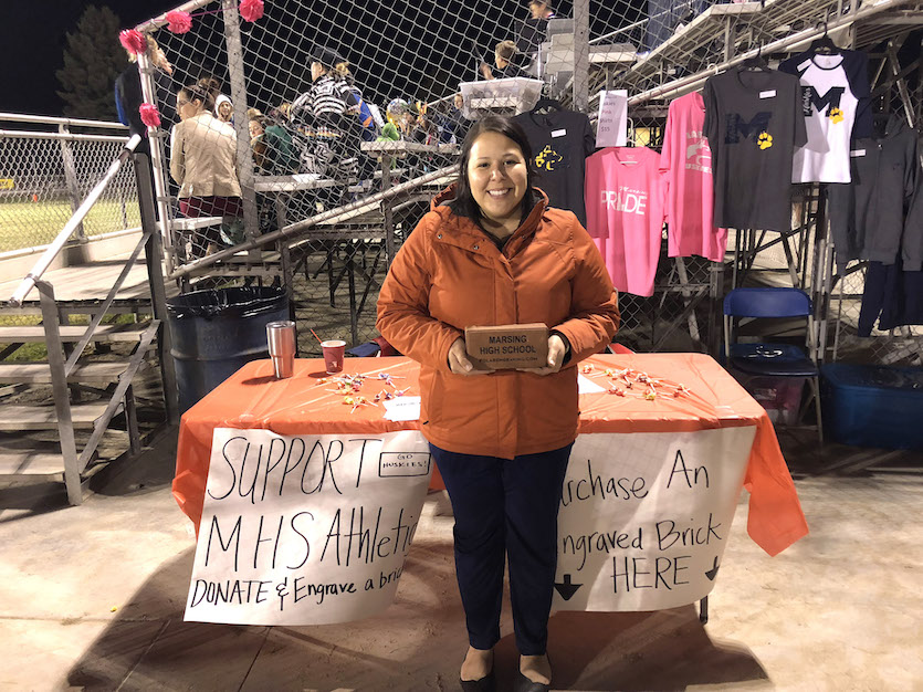 Photo of Angelo Pierce standing at a table raising money for bricks at a Marsing High School football game.