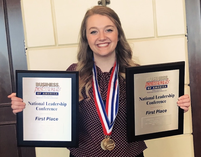 Photo of Kelsee Harrison holding up a plaque in each arm.