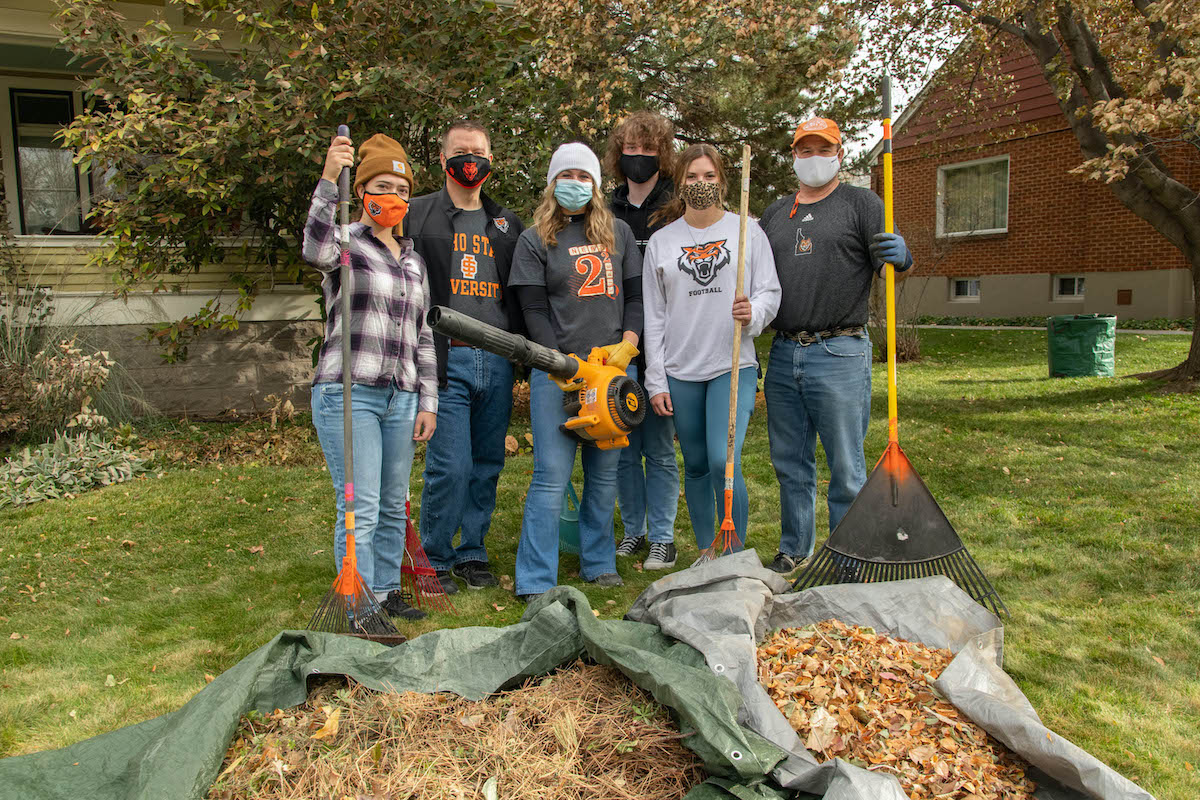 Students, president and mayor posing in front of leaves.