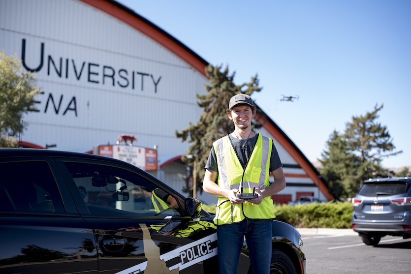 Photo of Lucas Rosa with drone controls standing by police car in front of Holt Arena.