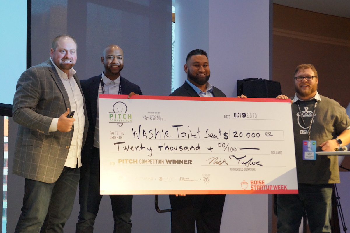 Prize winner holding giant check with officials standing near.