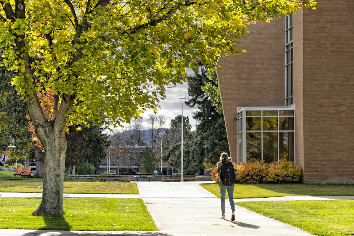 Student walking at ISU by trees in fall colors.