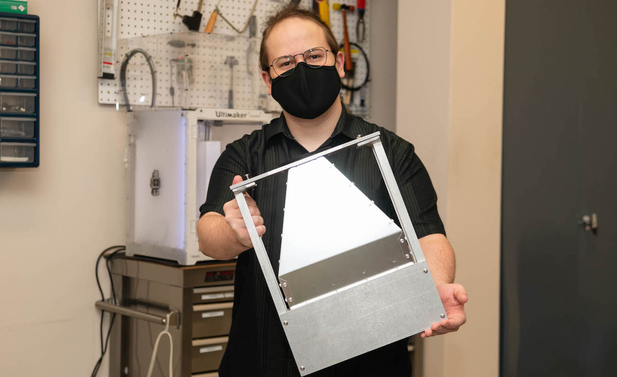 Alec Lepisto in McNuly lab, wearing a mask, holding device created in the lab