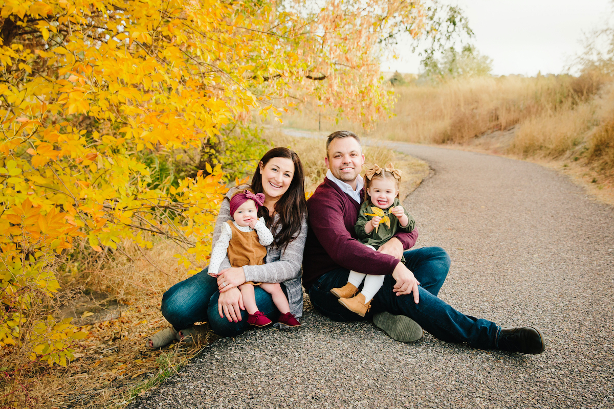 The Thompsons with their two young daughters on their laps with fall-colored trees in backgroun.