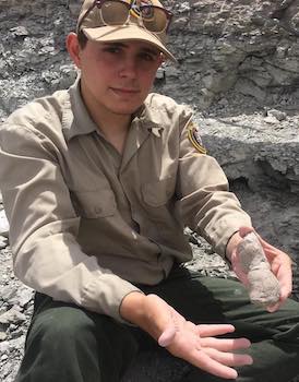 A photo of Xavier out in the field holding a fossil.
