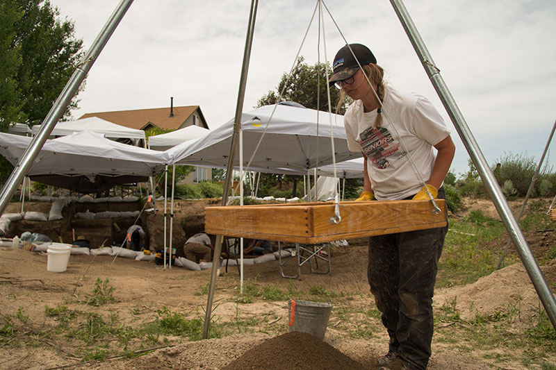 Student sifts dirt for fossil fragment