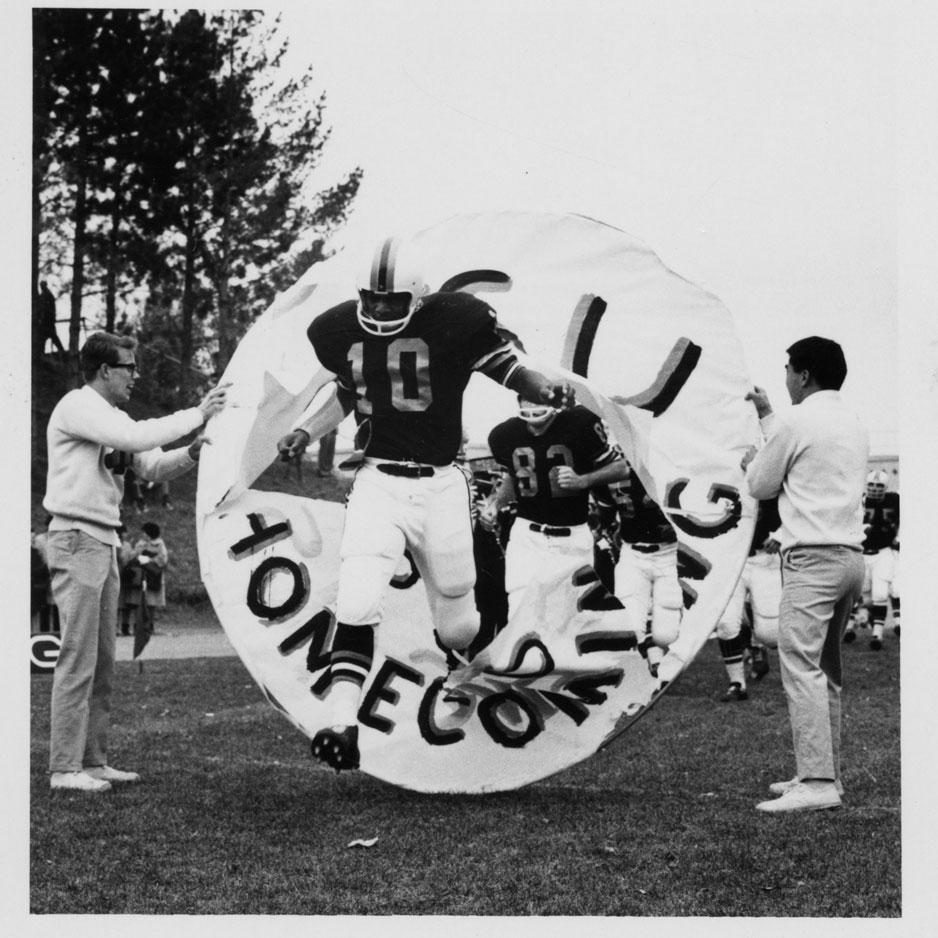 Early '60s photo of an ISU football player jumping through a homecoming banner