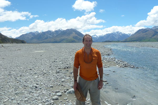 A man on a rocky shore with mountains in the background