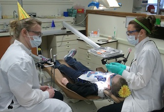 Junior student Shasta Chandler, left, and senior student Tiffany Colin, right, work on one of 91 children receiving exams during Give A Kid A Smile Day activities.